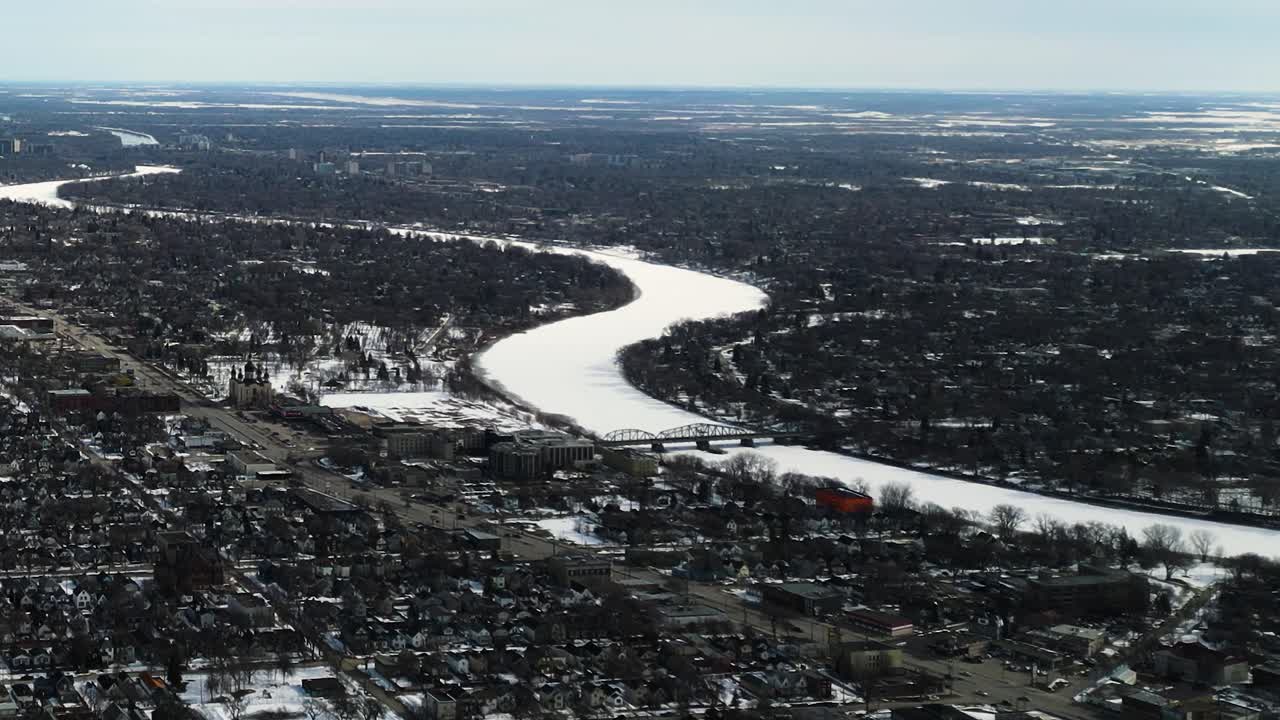 Drönarbild över den frusna Assiniboinefloden i Winnipeg, Manitoba, under våren, med snötäckt is som kröker sig bort i fjärran.