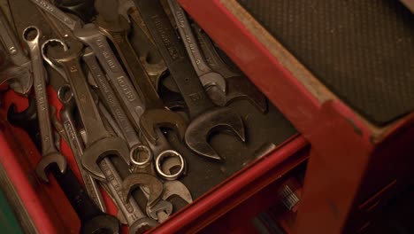 caucasian male hand opens drawer of a red tool cabinet, filled with various wrenches