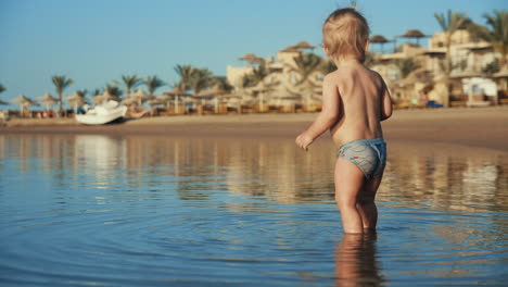 Joyful-child-walking-out-of-water-to-sea-coastline-in-summer-evening.