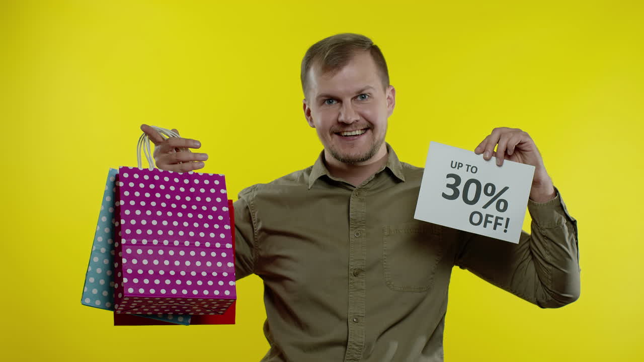 hombre mostrando hasta un 30 por ciento de descuento en inscripciones y bolsas de compras, pareciendo satisfecho con los bajos precios