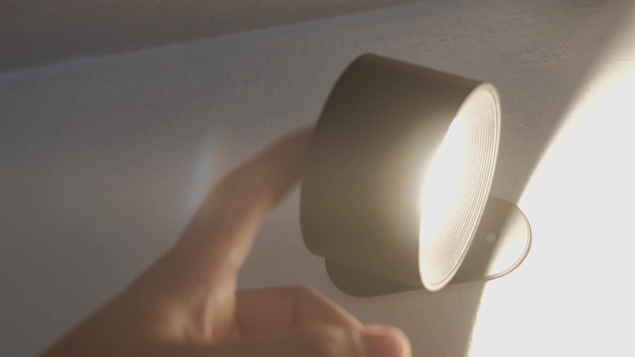 屋内壁掛けマウントから明るい磁気LED照明器具を消して取り外す手のクローズアップ静止画。