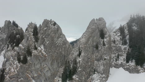 drone flying between mountains peaks in thick mist and revealing a beautiful snow covered valley