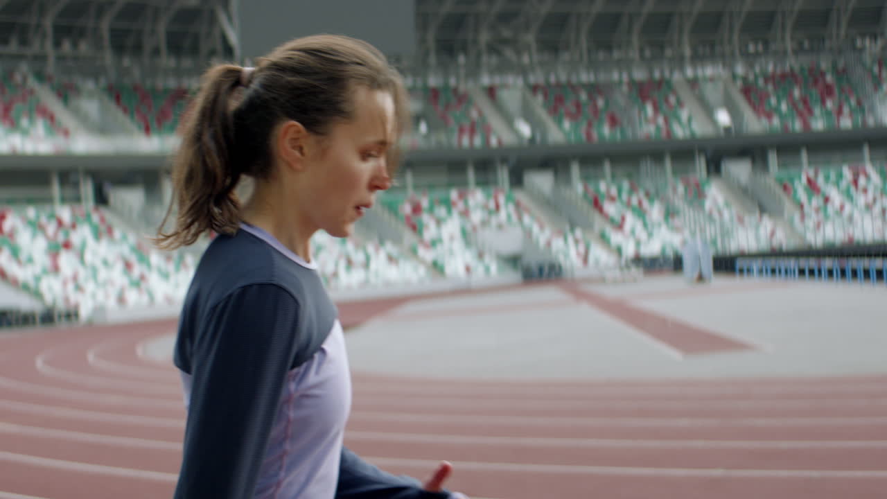 아침 일찍 빈 경기장 트랙에서 달리기 전에 따뜻해지는 백인 여성의 초상화. 아나모르픽 렌즈로 촬영