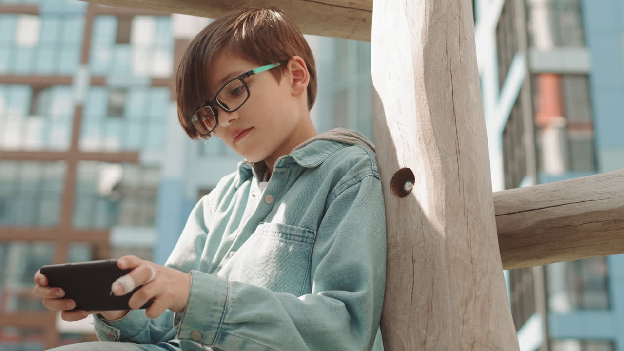 Caucasian Boy Playing Games on Smartphone Outdoors