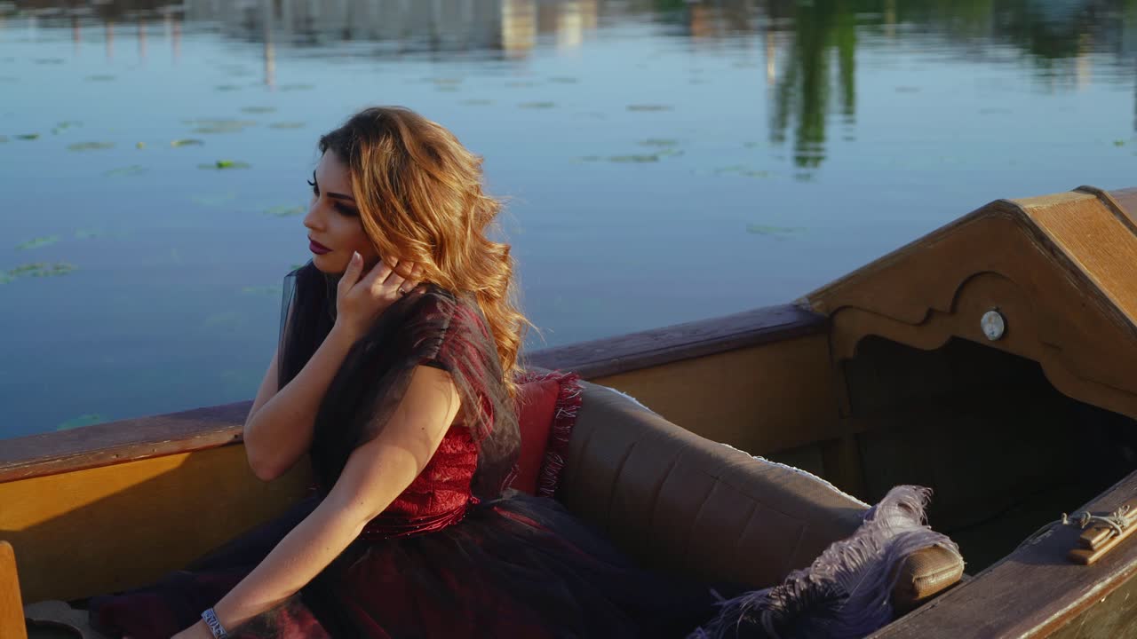 Luxury young woman wearing elegant carnival dress floating in gondola on the water background. Fantastic female with long hair and pretty makeup sitting in a boat.