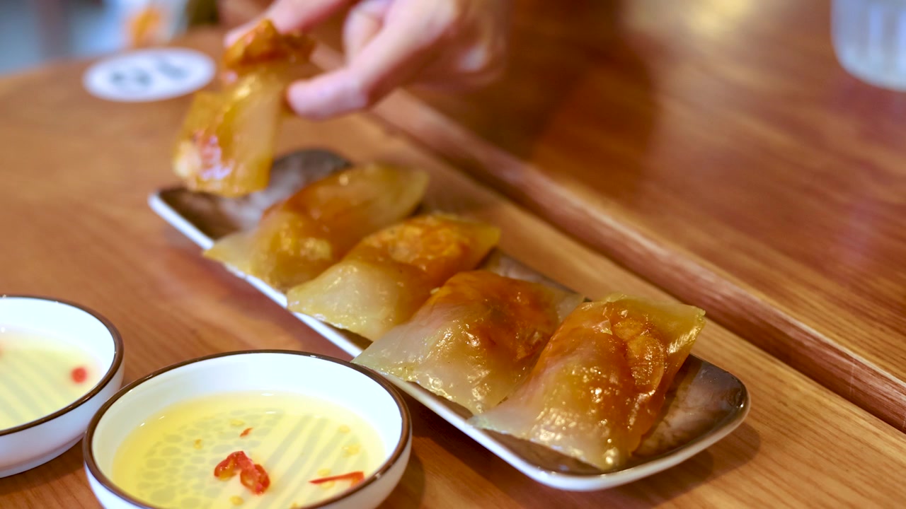 A person picks up a translucent tapioca dumpling from a plate on a wooden table