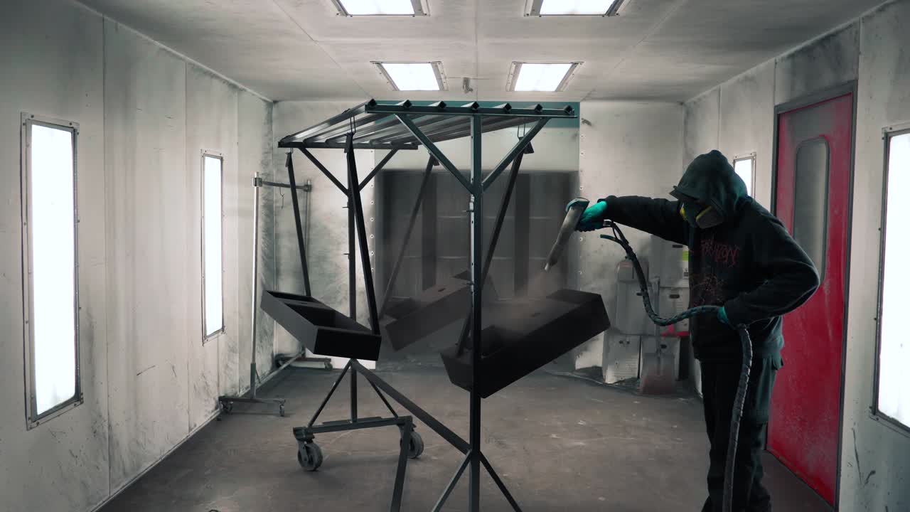 hombre que aplica un recubrimiento en polvo anticorrosión negro a una chapa metálica utilizando una pistola pulverizadora en la fábrica