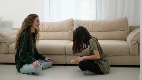 happy family of cute daughter and young mother having fun at home - girl throwing candies to mom's mouth