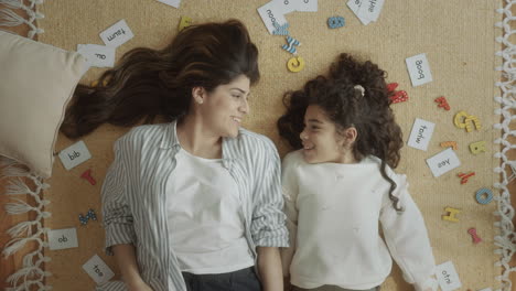 happy mother and daughter lying on the floor and waving at camera