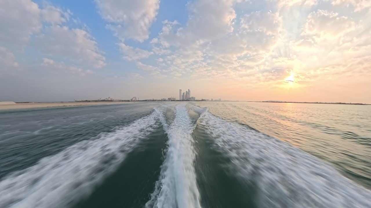 Experience the breathtaking view of Abu Dhabi's city skyline at sunrise in the United Arab Emirates from a speedboat looking over the wake capturing the serene water and vibrant sky