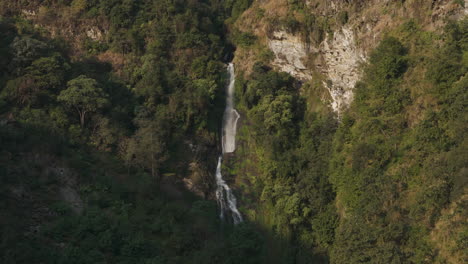 Landscape-Drone-shot-of-a-waterfall-in-Nepal,-into-the-wild-forest-with-hidden-honey-hive,-Natural-beauty,-showing-secret-life-of-bees-amidst-the-lush-greenery-and-rugged-terrain