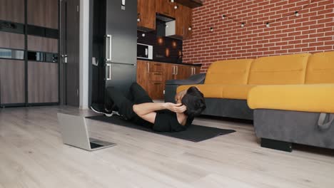 man training on mat with laptop at home, doing bicycle exercise on back