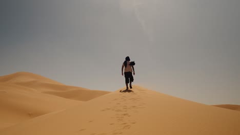 Person walks alone along the crest of a sand dune under the midday sun in Merzouga, Sahara Desert, Morocco