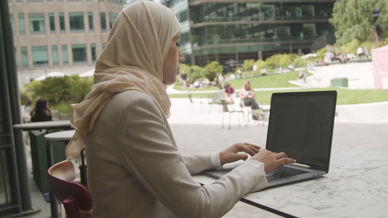 Muslim Businesswoman Sitting Outdoors In City Gardens Working On Laptop