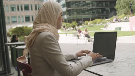 muslim businesswoman sitting outdoors in city gardens working on laptop