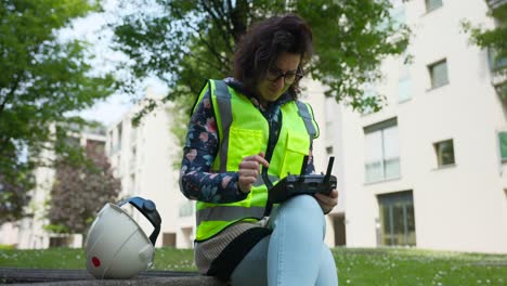 Female-Engineer-Checking-Remote-Controller-For-Aerial-Drone-Whilst-Sat-On-Bench