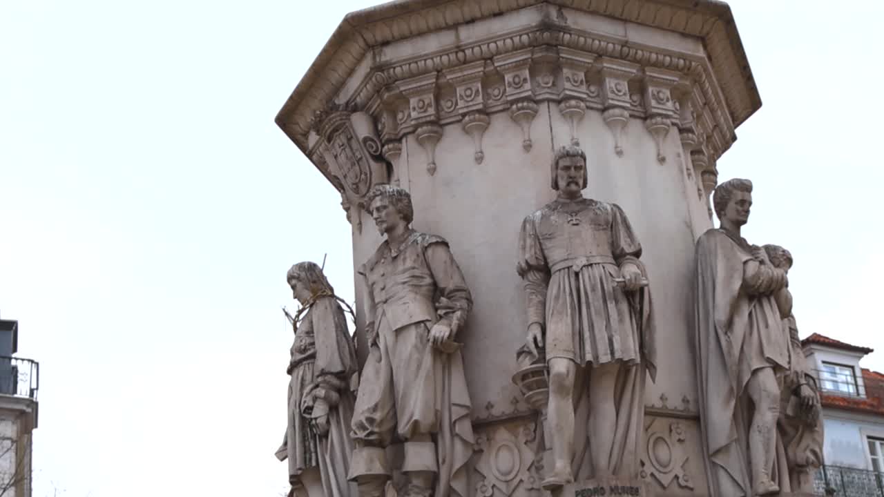 Vista cinematografica dal basso verso l'alto del monumento a Camões a Lisbona, che mostra statue storiche dettagliate su un cielo nuvoloso e luminoso nel centro della città