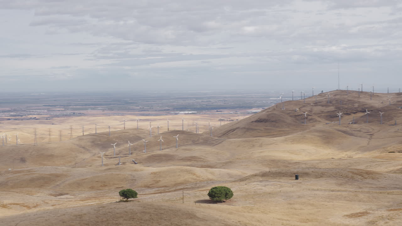 Ampia panoramica su colline aride coperte da pale eoliche in una giornata nuvolosa, alcune pale eoliche girano.
