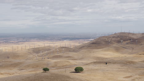 wide pan across dry hills covered in windmills on cloudy day, some windmills turn