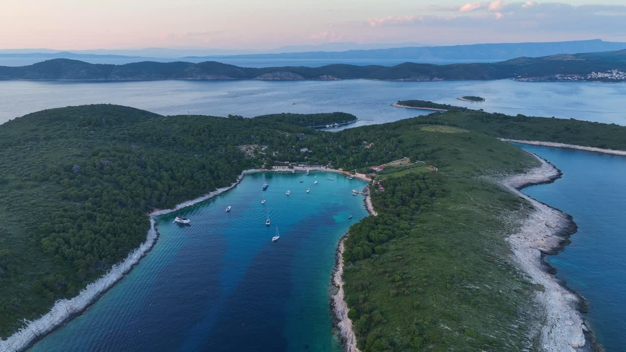Letecký záběr: Ostrov Hvar při západu slunce s Jaderským mořem, loděmi a lesem v Chorvatsku, kruhový záběr dronem.