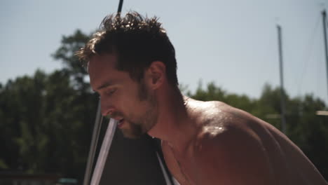 Young-man-climbing-onto-yacht-deck-from-water,-after-jumping-in-river