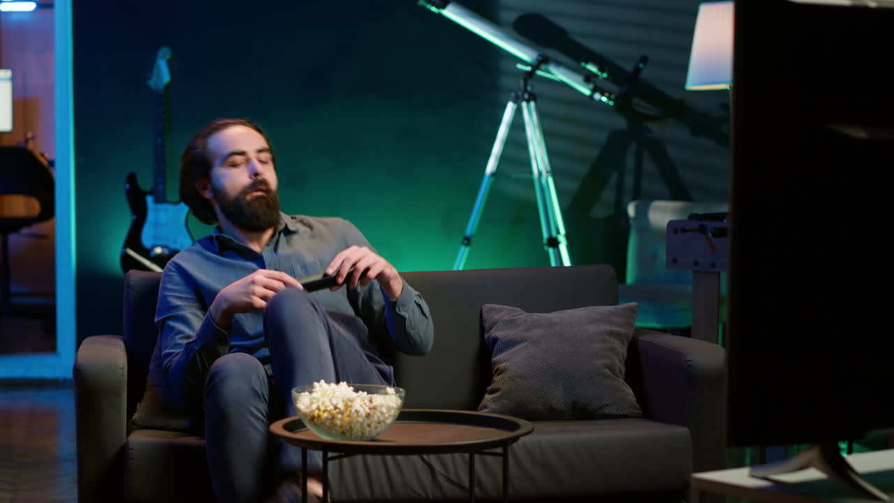 집에 도착한 남자가 tv에서 영화를 보는 동안 소파에서 휴식을 취하고 있습니다.