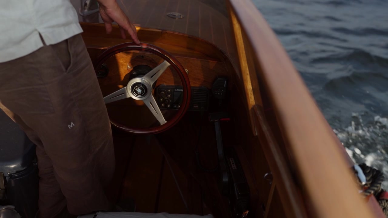 Close up of a person navigating a classic mahogany motorboat across the ocean. Authentic lifestyle and luxury travel concept during a cinematic sunset.