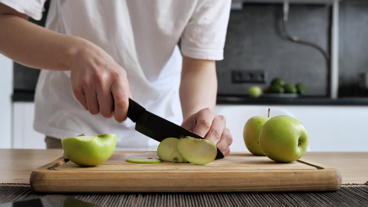 niña cortando manzana verde en rebanadas en una tabla de bambú en la cocina