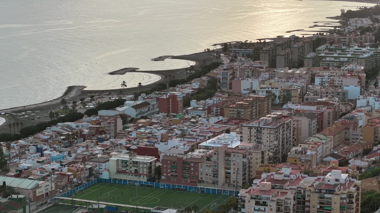 Aerial view of Málaga city and coastline, Andalusia, Spain. Urban architecture, coastal buildings, and curved promenades along the Mediterranean Sea under the warm evening light