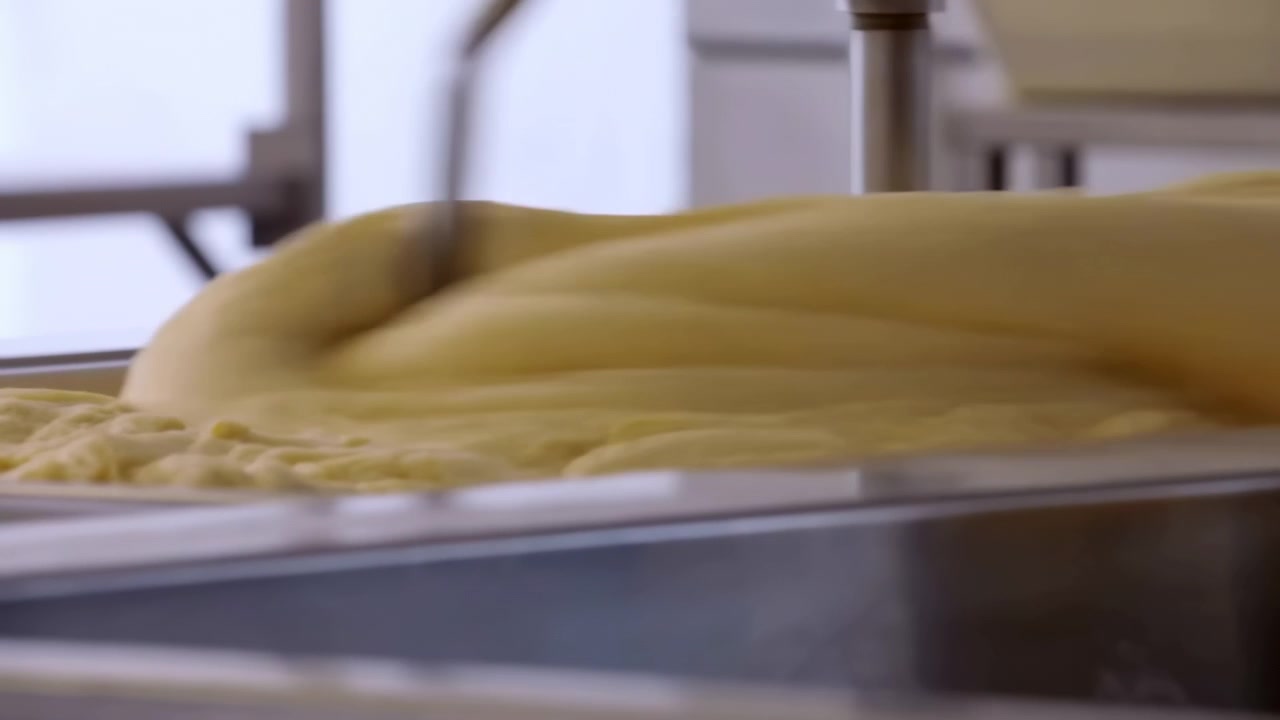 Adonan Roti Industri Mengalir di Bawah Nosel, Close-up Adonan Kuning yang Keluar ke Nampan Stainless, Konveyor