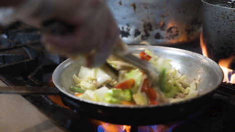 Chef-uses-tongs-to-stir-fry-vegetables-in-pan-over-high-heat-flames-in-commercial-restaurant-kitchen,-close-up-HD
