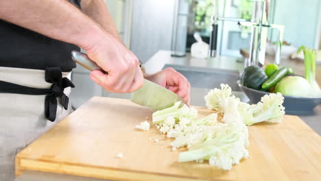 chef masculino cortando la coliflor con la punta del cuchillo afilado en su cocina