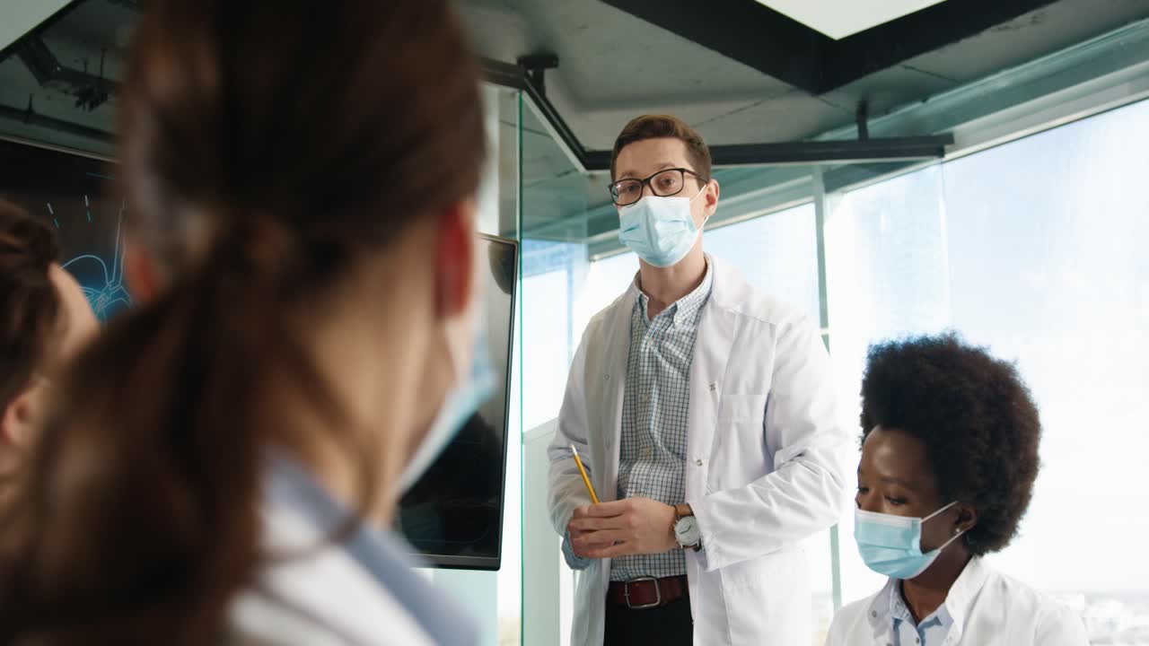 Bottom view of male doctor in mask discussing with multi-ethnic doctors team statistics of coronavirus lung disease in hospital while they observing at digital monitor