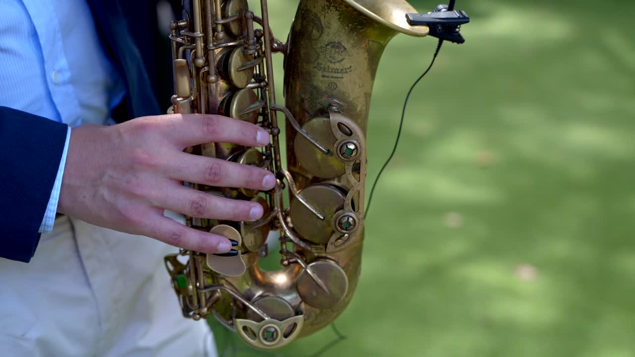 Saxophonist holding a brass saxophone outdoors, with a microphone attached to the instrument