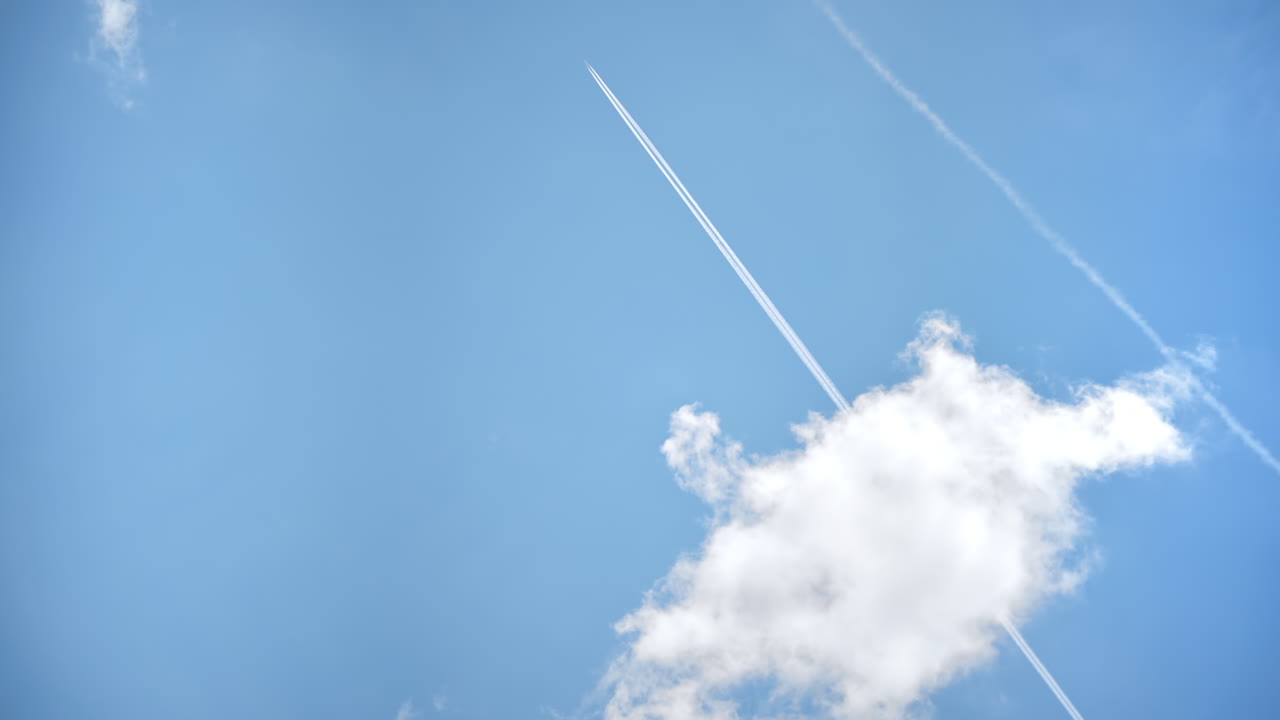View of the partly cloudy sky with flying plane in the distance leaving a trail