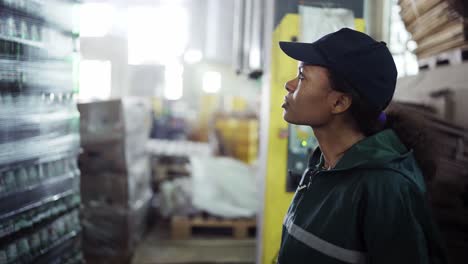 and african-american woman in a special green uniform monitors the process of packaging raw materials at a waste processing plant