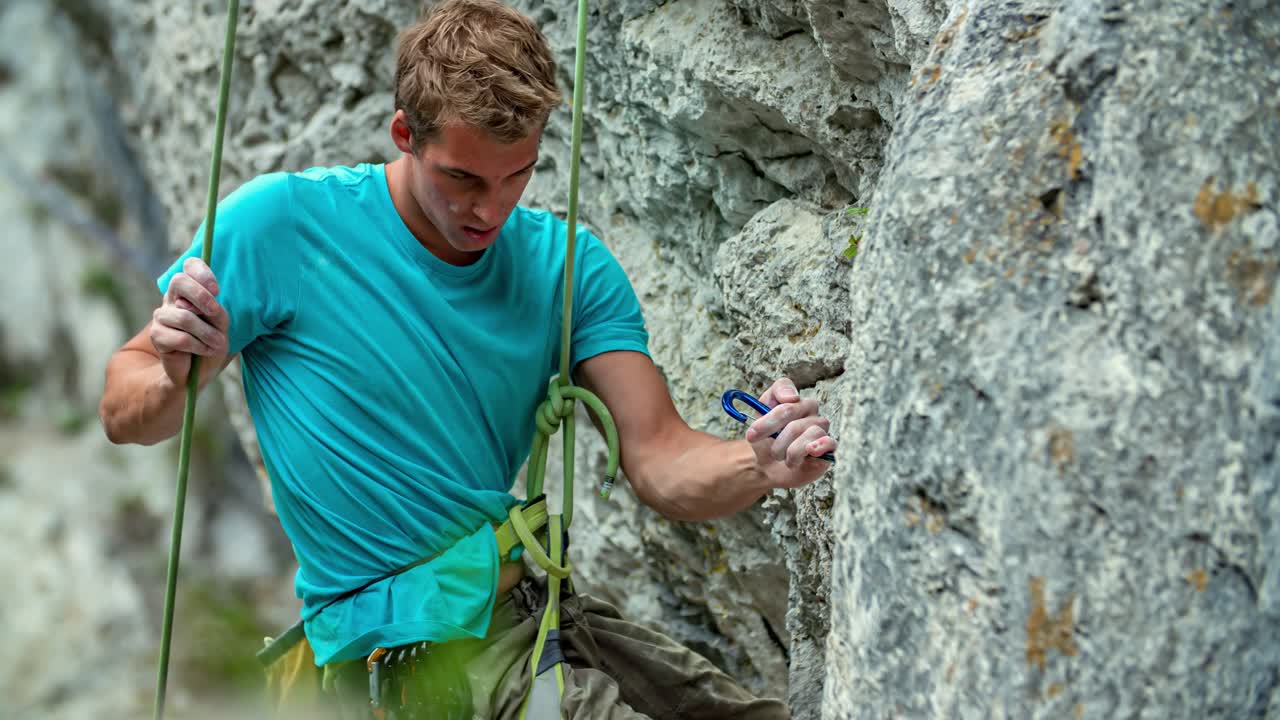 Young strong Caucasian man rock climber stands, unclips and holds on to mountainside, close up