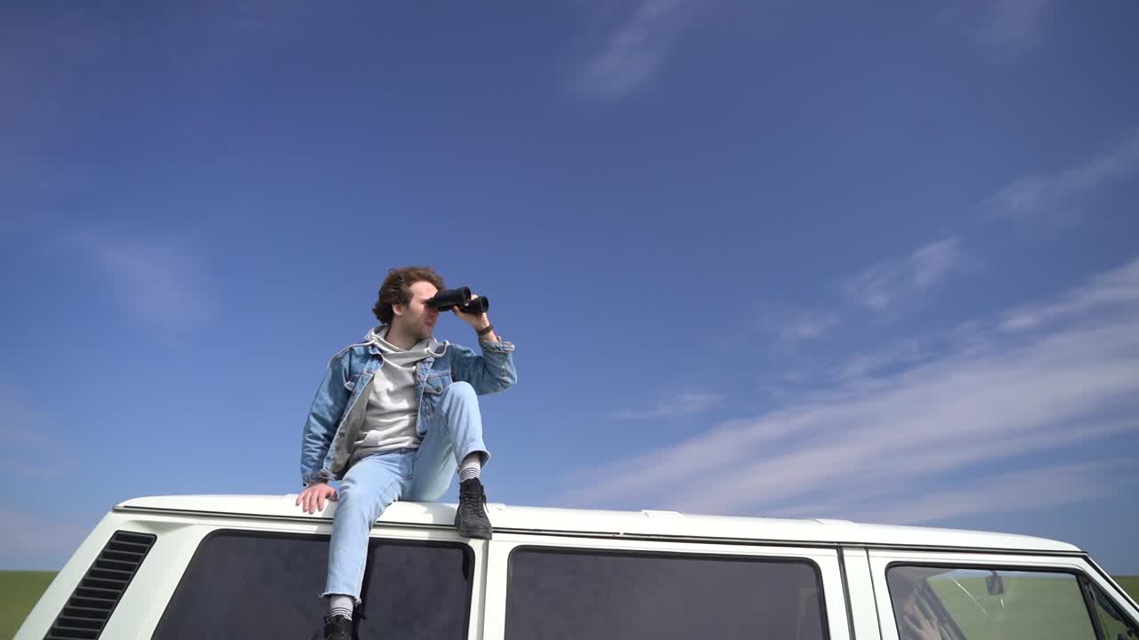 Young boy looks around with a pair of binoculars on the roof of a caravan.