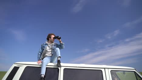 young boy looks around with a pair of binoculars on the roof of a caravan.