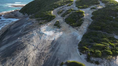 Aerial-shot-of-bikers-and-their-dog-riding-over-the-rocks-at-Wylie-Bay-Rock-Beach