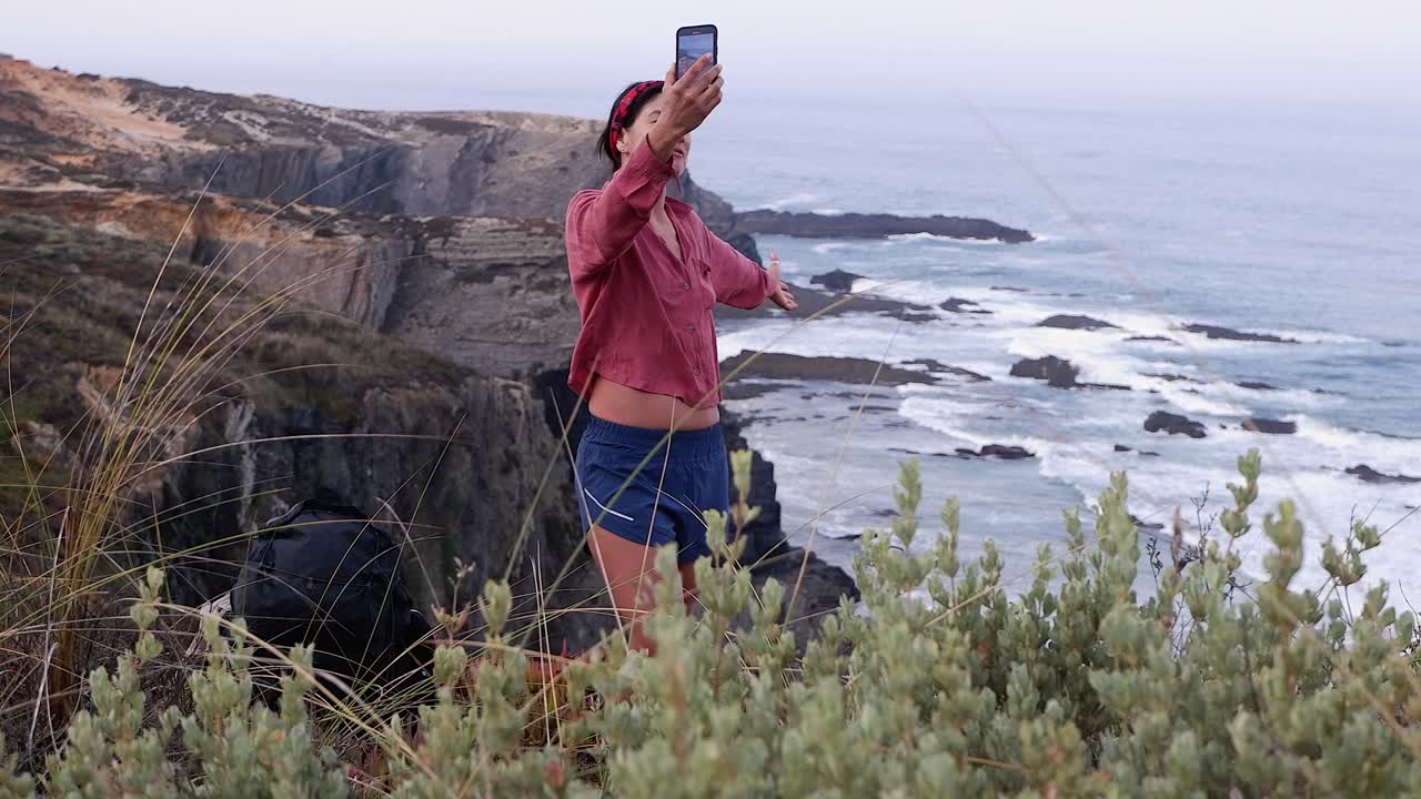 Hispanic woman on top of rugged ocean cliffs makes social media post