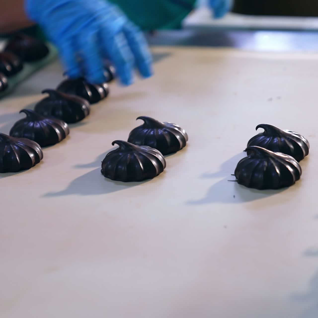 Hands in blue gloves take away marshmallows from the conveyor belt. Chocolate zephyr candies being packed into boxes. Close up