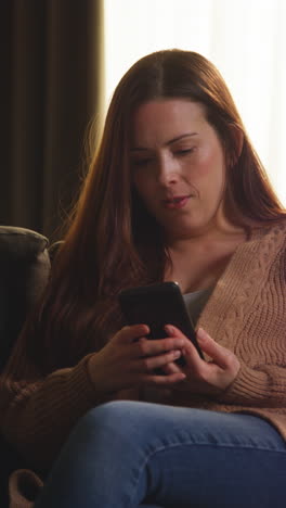 Vertical-Video-Of-Woman-Sitting-On-Sofa-At-Home-At-Streaming-Or-Watching-Movie-Or-Show-Or-Scrolling-Internet-On-Mobile-Phone-1