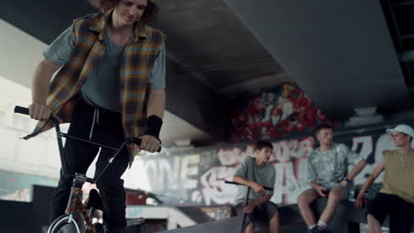 active man practicing bmx bicycle at skate park with graffiti on wall.