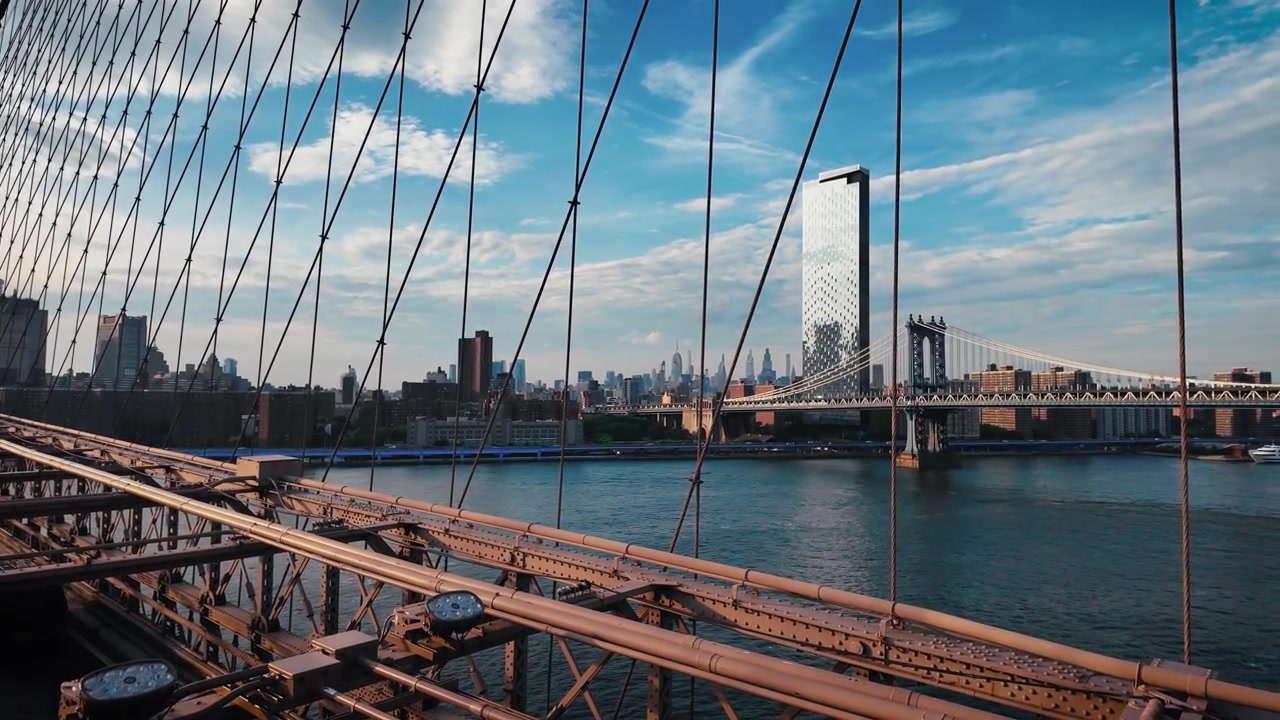 Vista all'ora d'oro dal Ponte di Brooklyn con il Ponte di Manhattan, l'East River e lo skyline di Lower Manhattan sotto nuvole drammatiche, creando un paesaggio urbano cinematografico di New York