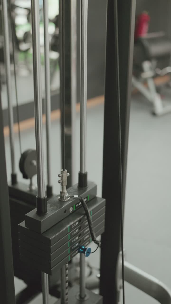 Close up of weight stack and cable system on gym machine showing metal plates and adjustment pin in fitness center vertical framing