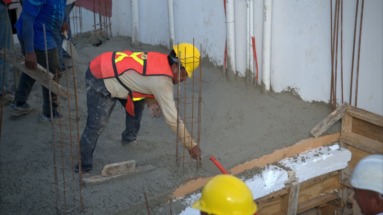 movimiento lento de un trabajador de la construcción latino mexicano con un casco y un chaleco naranja aplanando el hormigón fresco usando una paleta