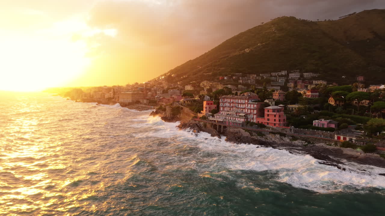 Sunset over coastal town with waves crashing onto rocky shore