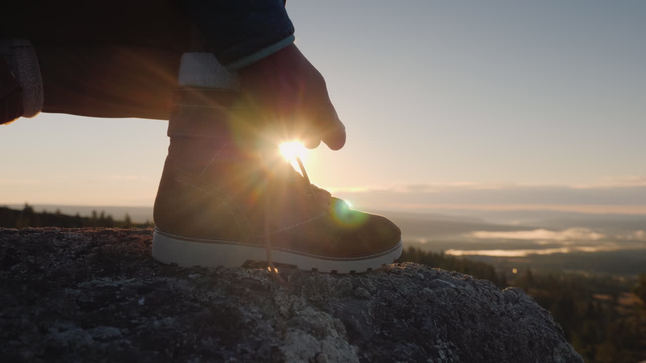 여행자는 산꼭대기에서 뒤를 배경으로 신발끈을 끈으로 묶는다