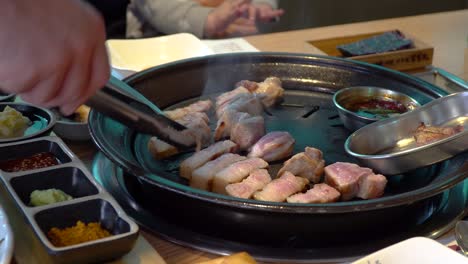 hands turning pork belly on traditional korean bbq named samgyeopsal